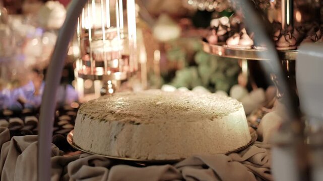 Traditional halva cake topped with pistachios displayed on a dessert table at a festive event. Static close up.
