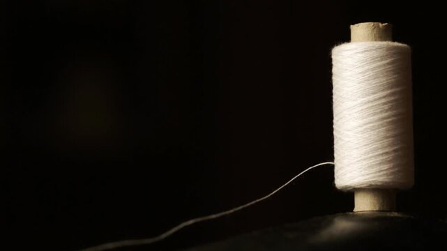 A spool of white thread stands on a retro sewing machine, seamstress
