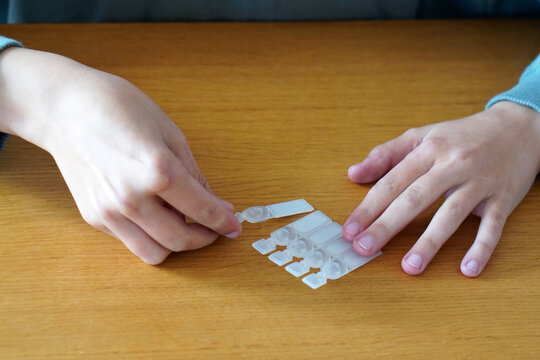 Medication in adolescence. A teenager opening a vial of eye drops for their irritated eyes.