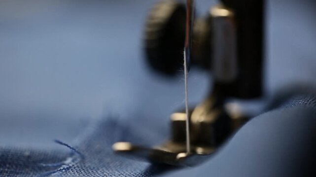 A tailor sews denim fabric on a sewing machine, close-up view