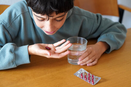 Medication and self-medication in adolescence. A teenager taking a red pill with a glass of water