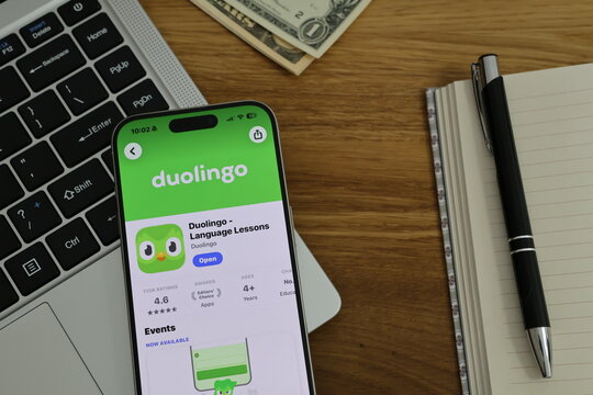 Kiel, Germany - 02-25-2026: A smartphone displaying the Duolingo language learning and practice app in App Store displayed on smartphone placed on top of laptop on wooden desk