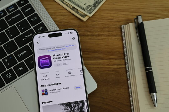 Kiel, Germany - 02-25-2026: A smartphone displaying the Final Cut Pro professional video editing app in App Store displayed on smartphone placed on top of laptop on wooden desk