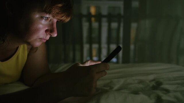 Young Woman Lying in Bed at Night Using Smartphone for Reading News and Browsing Social Media
