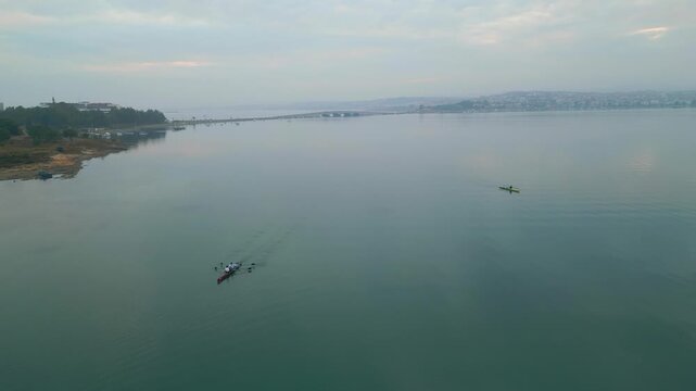 Two Kayaks Paddling Near Quiet Shoreline Under Soft Morning Sky, Aerial View Shows Small Wakes And Coastal
