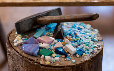 Primo piano di un martello appoggiato su un tronco di legno contenente colorate tessere di un futuro mosaico 