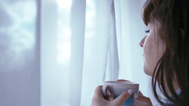 Serene Coffee Moment: Woman Relaxing with a Cup by the Window on a Cloudy Day