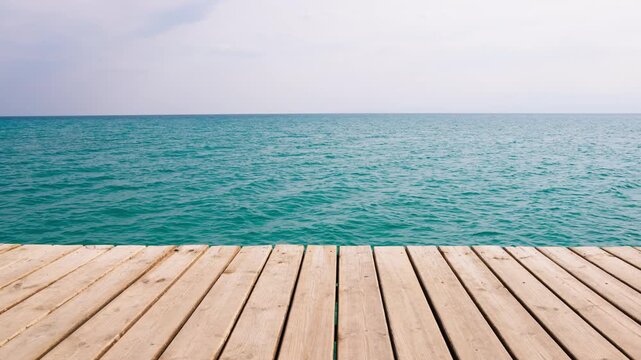Wooden dock planks extend over calm turquoise waters of Issyk-Kul Lake, leading to the endless blue horizon under a clear sky. Serene summer landscape in Kyrgyzstan.