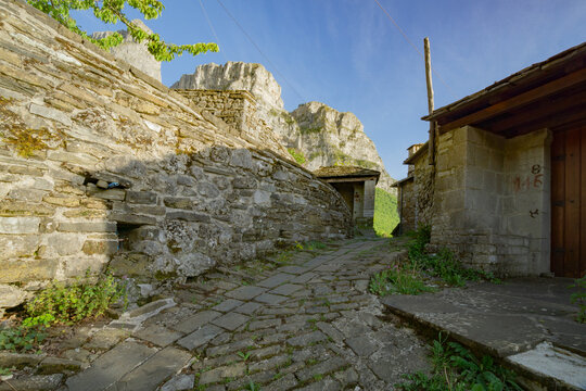 View of a stone-paved path weaving through aged stone buildings under a vast sky, contrasting with rugged rock formations in Mikro Papigko, Ioannina, Greece.