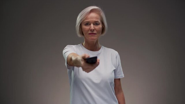 Old woman hand holding tv remote control. Elderly female presses button of device and turns channel, switching surfing. Senior lady with grey hair turn off on television. Recreation and entertainment