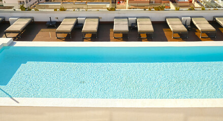 Obraz premium Sunlit rooftop hotel pool with sparkling turquoise water and empty loungers. For travel, real estate, wellness, hospitality and lifestyle branding.