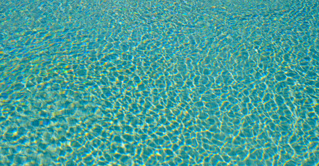 Crystal clear turquoise swimming pool water with sunlit ripples. Abstract summer background for wellness, relaxation, spa, travel and resort advertising.