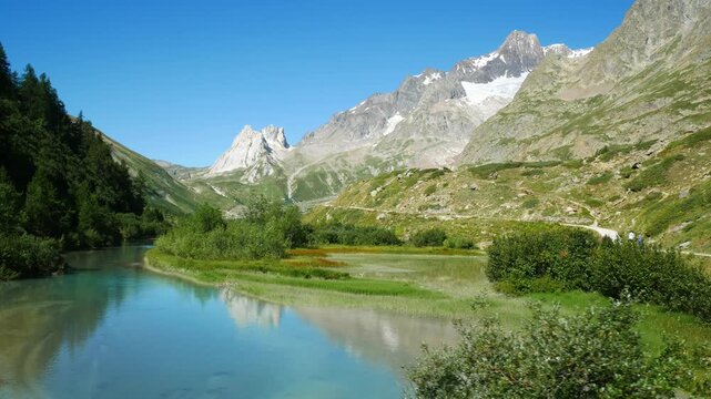 Panoramic view of the Veny Valley, Aosta Valley, Italy. Calm reflecting waters of a mountain lake in the foreground. Alps mountain chain with blue sky on the background.