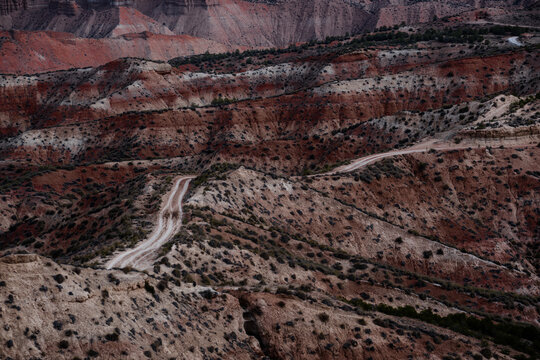 View of winding dirt road snakes through arid, multi-layered landscape, where earthy reds and browns meet sparse greenery, Gorafe, Andalucia, Spain.