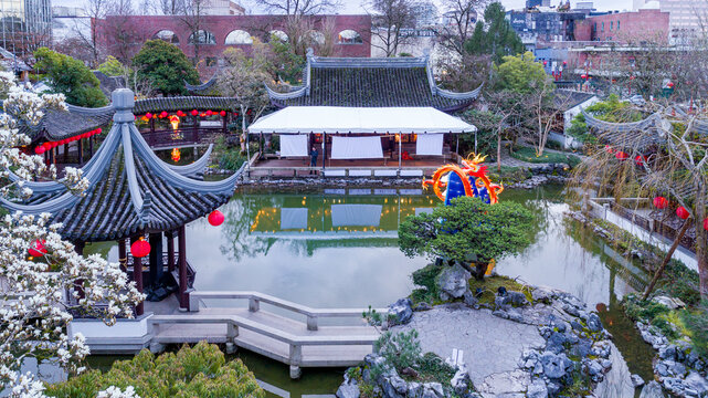 View of a tranquil pond reflecting traditional Chinese architecture, lanterns casting a warm glow, and lush greenery creating a serene escape, Portland, Oregon, United States.