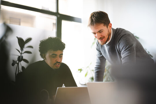 Two men collaborate on a project, looking at a laptop screen in a modern office setting.