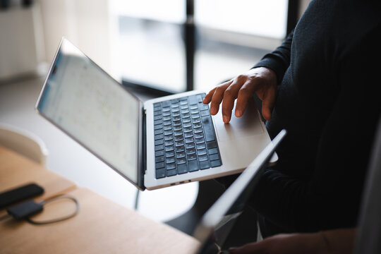 A person's hand rests on a laptop keyboard, interacting with a map displayed on the screen. The scene suggests remote work or planning.