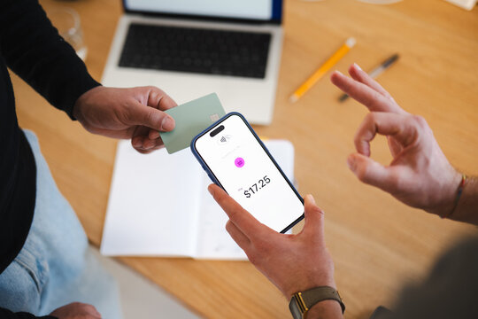 A person holds a credit card while another person uses a smartphone for a contactless payment of $17.25.