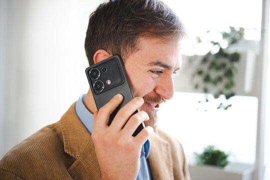 A man in a corduroy jacket talks on his mobile phone, smiling as he engages in a conversation.