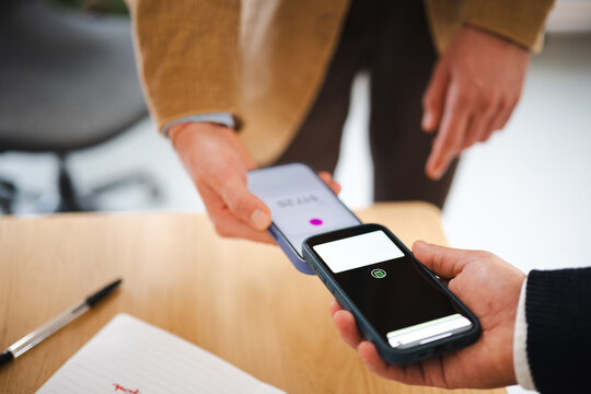 Two people are using their mobile phones to make a contactless payment. One phone is held close to the other, indicating a transaction is in progress.