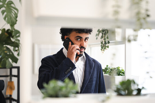 A man in a suit jacket and striped shirt talks on his phone while looking at the camera.