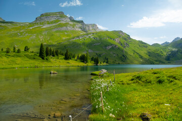 Obraz premium Discover the beauty of Engstlensee Lake in Switzerland. Clear waters reflect surrounding mountains and greenery, showcasing a serene natural landscape. Travel destination and popular trail.