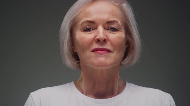 Portrait: old woman takes a deep breath, she inhales deeply and smiles. Senior female face with gray hair, beautiful wrinkles. Peace and happiness. Blue eyes, white shirt. Taking care of mental health