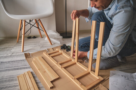 Man assembling new flat-pack wooden furniture on a cardboard box at home