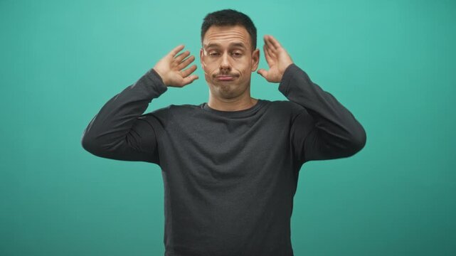 Man holding hands to head and shrugging shoulders in studio teal backdrop, face with smirk and dismissive expression; exasperation.