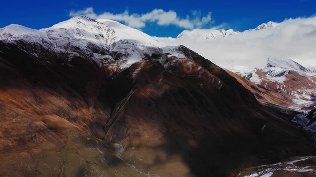 drone view of snowcapped summit under deep blue sky, steep flanks and glacial patches visible, sharp contrast between white snow and brown slopes conveys high elevation clarity and pristine alpine