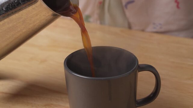 a person pours hot coffee from a moka pot into their cup