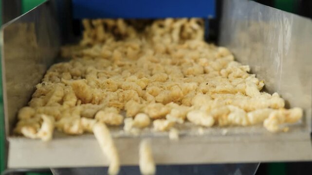 Close-up of an industrial machine extruding a grain mixture, creating puffed cereal snacks on a vibrating conveyor belt during the food manufacturing process in a factory plant