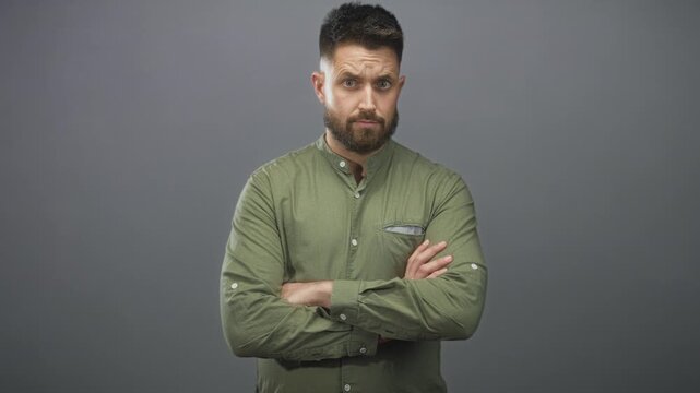 Bearded man with arms crossed and furrowed brow wearing green button shirt in studio; reserved skepticism caution.