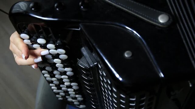 Close-up detail of woman hand skillfully pressing white buttons on a shiny black accordion, creating musical notes. Performance by musician during practice session, showcasing instrument intricate det
