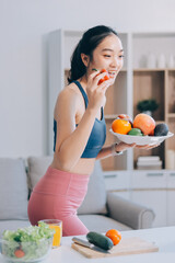Fit young Asian women in activewear sitting on yoga mat and eating fresh vegetable salad after workout, representing clean eating, fitness lifestyle, wellness routine and health balance.