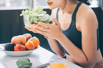 Fit young Asian women in activewear sitting on yoga mat and eating fresh vegetable salad after workout, representing clean eating, fitness lifestyle, wellness routine and health balance.