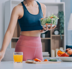 Fit young Asian women in activewear sitting on yoga mat and eating fresh vegetable salad after workout, representing clean eating, fitness lifestyle, wellness routine and health balance.