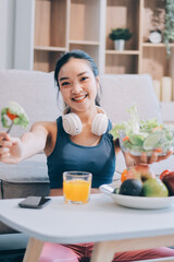Fit young Asian women in activewear sitting on yoga mat and eating fresh vegetable salad after workout, representing clean eating, fitness lifestyle, wellness routine and health balance.