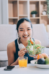 Fit young Asian women in activewear sitting on yoga mat and eating fresh vegetable salad after workout, representing clean eating, fitness lifestyle, wellness routine and health balance.