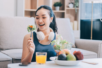 Fit young Asian women in activewear sitting on yoga mat and eating fresh vegetable salad after workout, representing clean eating, fitness lifestyle, wellness routine and health balance.