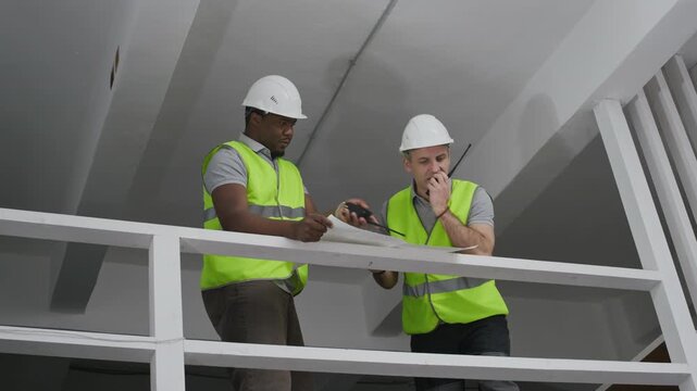 Low angle view of diverse male builders with blueprint and walkie-talkie working together at indoor renovation site