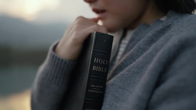 A happy woman praying and worship with Holy Bible at sunset for Christian faith, spirituality, devotion, hope, and religious belief. pray to god and religion concept	