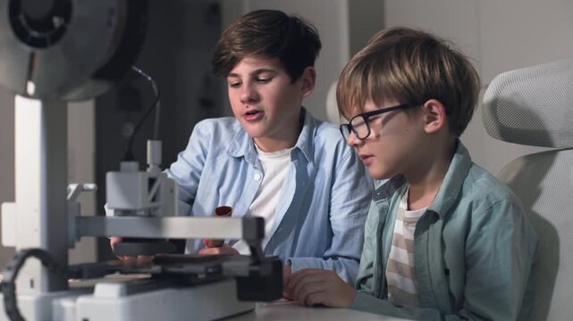 Two schoolchildren print parts on a 3D printer set up on a table
