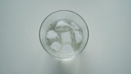 グラスに浮かぶ氷と炭酸の泡 真上からの俯瞰 爽やかな水のテクスチャ / Ice cubes in glass with soda bubbles, top view of refreshing water texture