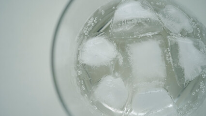 グラスに浮かぶ氷と炭酸の泡 真上からの俯瞰 爽やかな水のテクスチャ / Ice cubes in glass with soda bubbles, top view of refreshing water texture