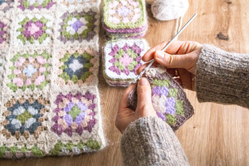 Close up of hands joining granny squares into one fabric. Crochet project in progress. Craft process, handmade fashion creation and slow creative lifestyle concept.  © Ina