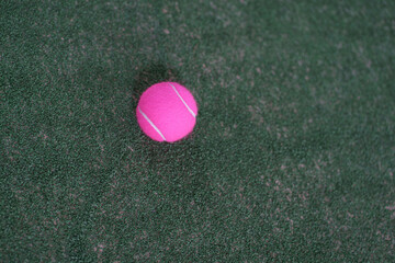 Pink tennis ball on green synthetic turf court. High contrast sports equipment for padel or tennis training.