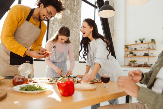 Group of positive men and women cooking together making dinner in modern stylish kitchen at home
