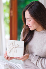 Vertical portrait image of a woman in sweater holding and looking at a present box at home