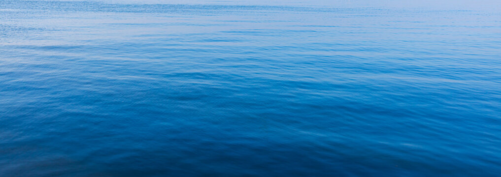 Blue water surface with gentle ripples and soft light reflection,An abstract top-down view of calm blue water surface. The image shows gentle ripples and a soft color gradient from deep blue to light 